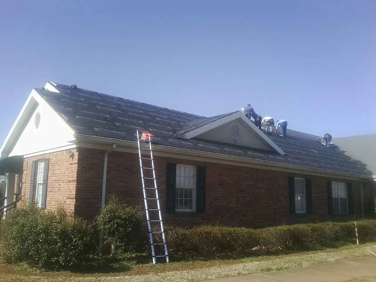 Crew tearing shingles off a brick ranch roof with a ladder set — Metal Roof Repair work by our crew in Carversville