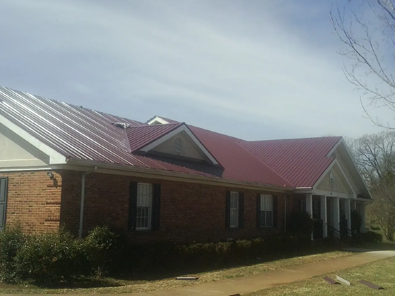 Red metal roof with gabled entries on a long brick building, from a Hail Damage Roof Repair job in Carversville