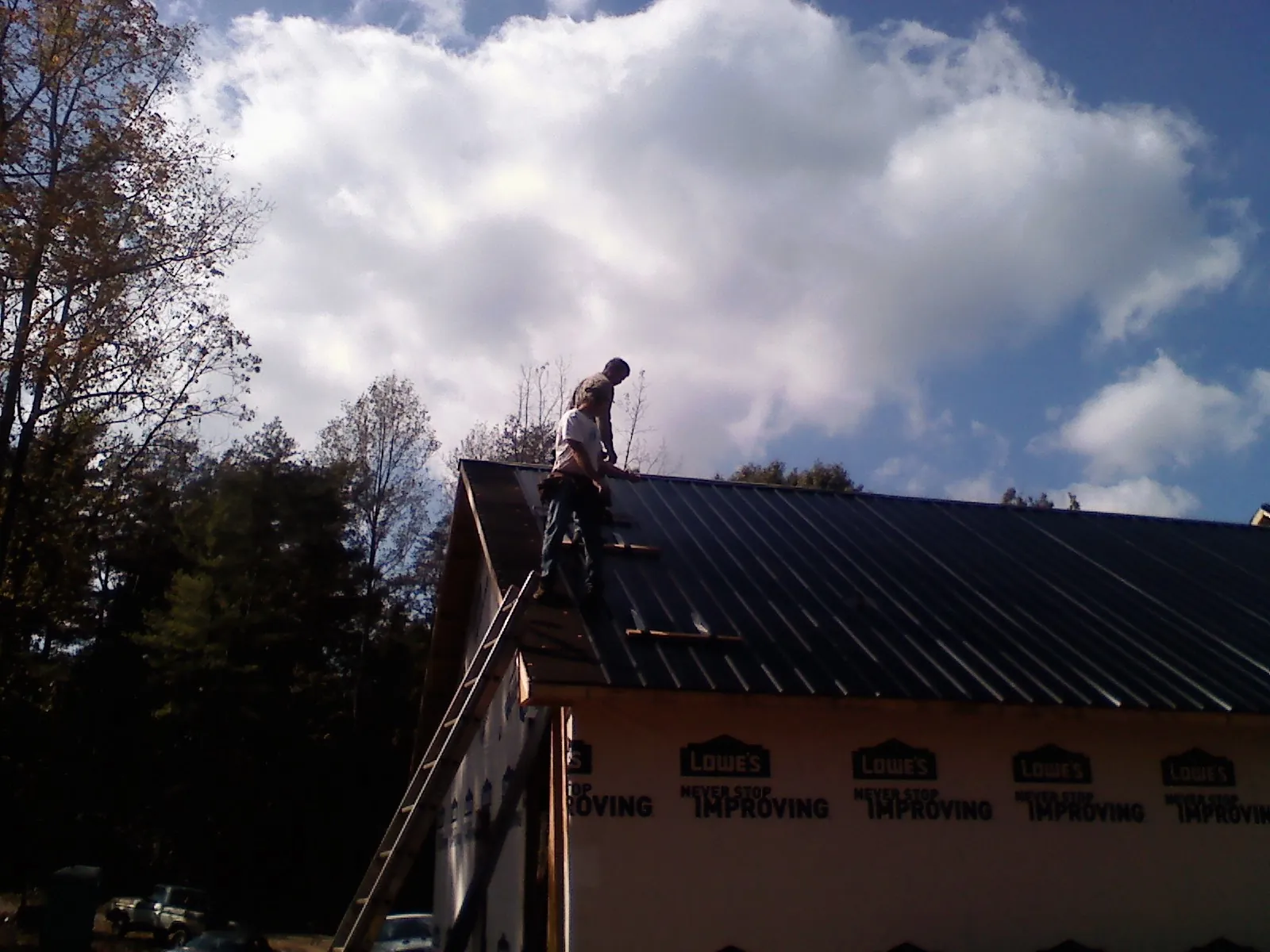 Roofer fastening dark metal panels high against a cloudy sky, from a Roof Inspection job in Carversville