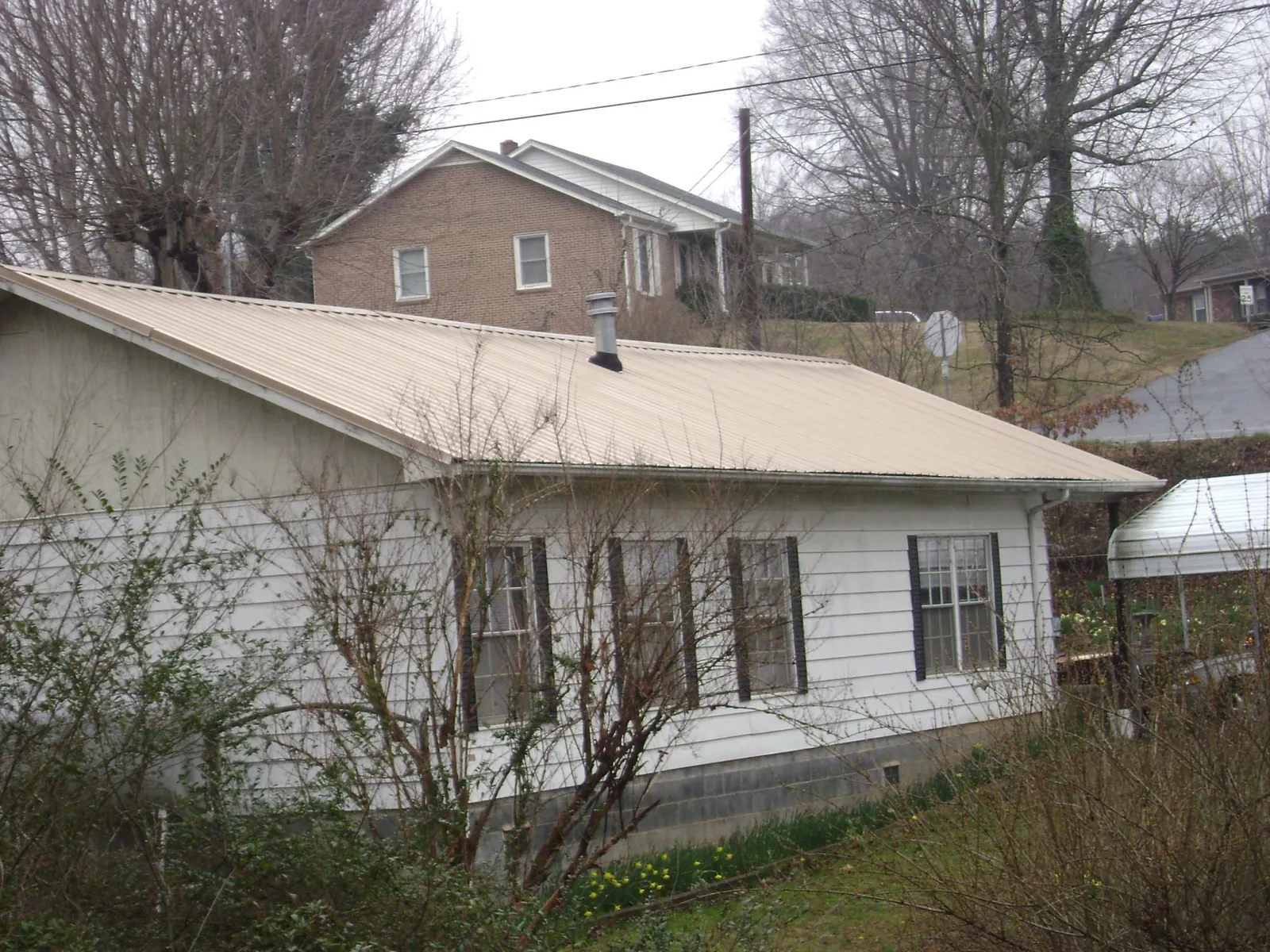Tan metal roof on a white sided house set into a hillside — Commercial Roofing by Roofing Brothers in Carversville